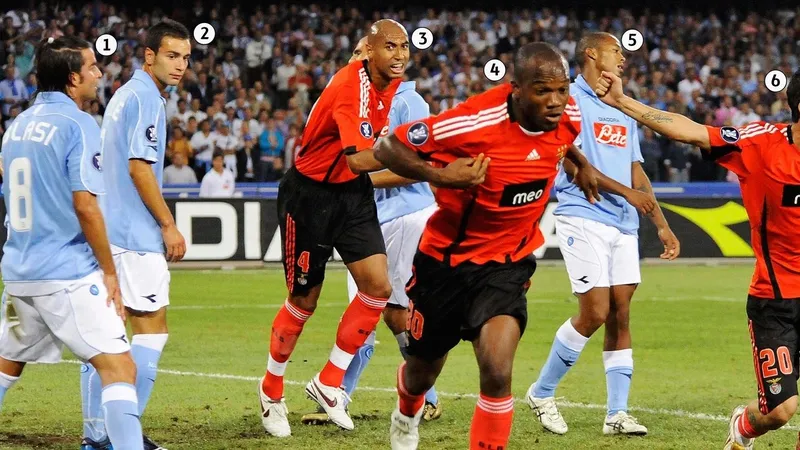 Cầu thủ Benfica với áo đỏ đang chống đỡ cầu thủ Napoli với áo xanh trên sân cỏ Cầu thủ Benfica với áo đỏ đang chống đỡ cầu thủ Napoli với áo xanh trên sân cỏ